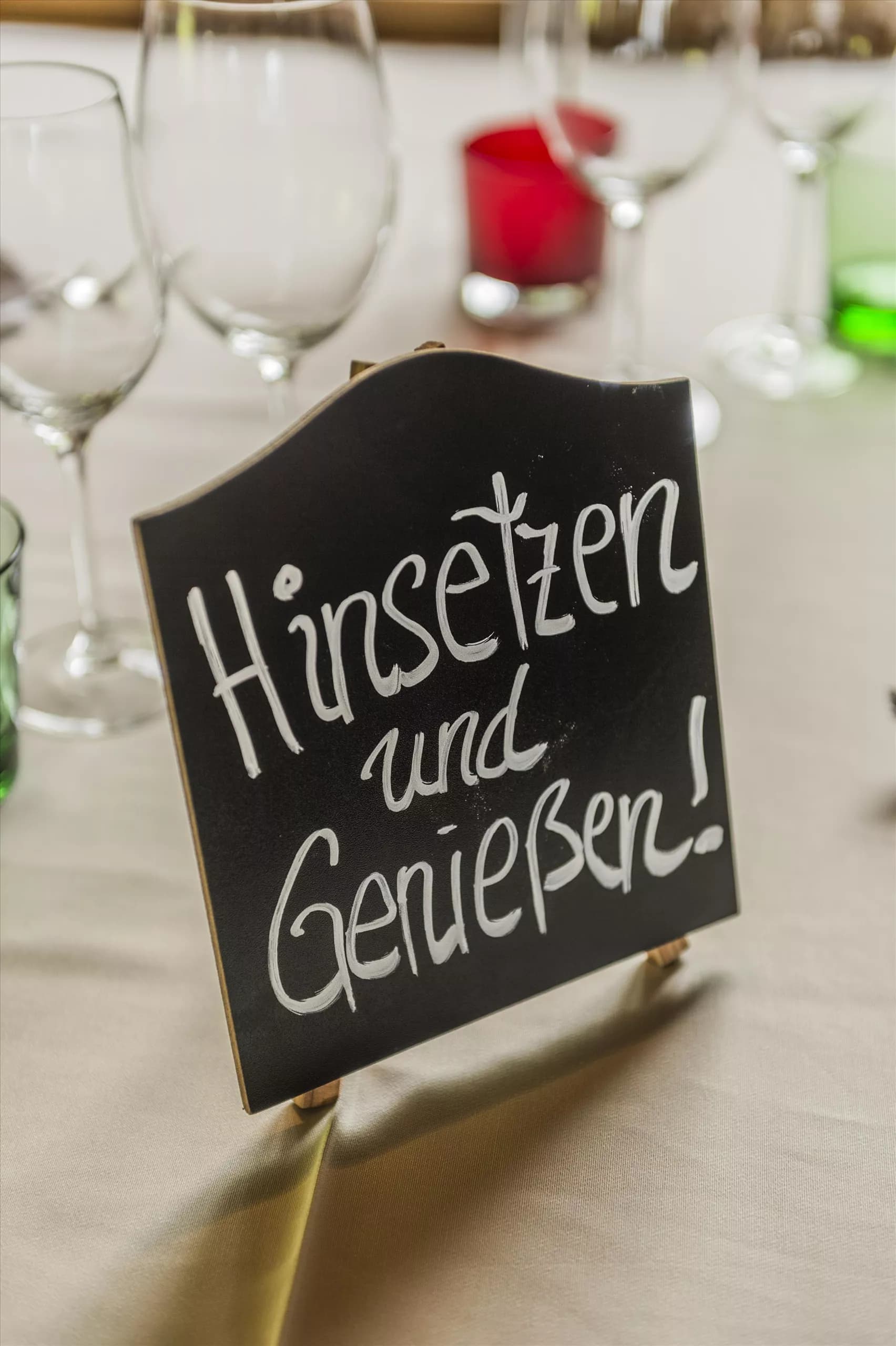 A stylish table setting with glasses and colorful candles. A sign invites with "Sit down and enjoy!"