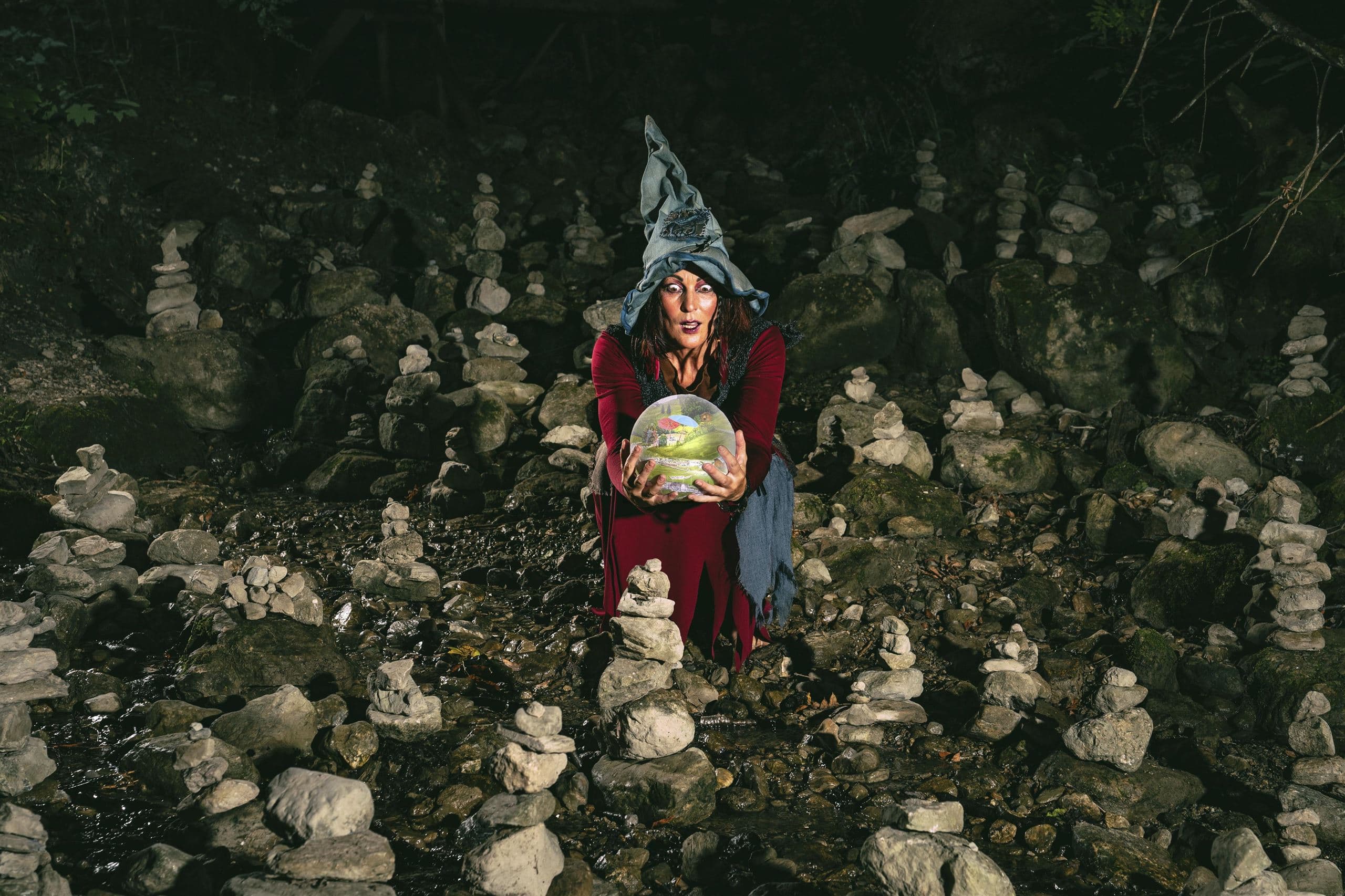 A mystical woman is wearing a magic hat and holding a glowing sphere. Around her, there are many stone turrets that create a mysterious atmosphere.